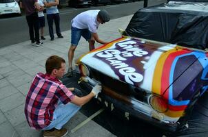 kharkov, ucrânia - 27 de maio de 2017 festival de arte de rua. jovens desenham grafite na carroceria do carro no centro da cidade. o processo de desenhar graffiti colorido em um carro com latas de aerossol foto