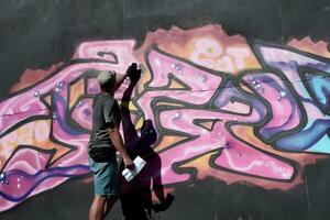 jovem caucasiano masculino grafite artista desenhando grande rua arte pintura dentro azul e Rosa tons foto