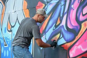 jovem caucasiano masculino grafite artista desenhando grande rua arte pintura dentro azul e Rosa tons foto