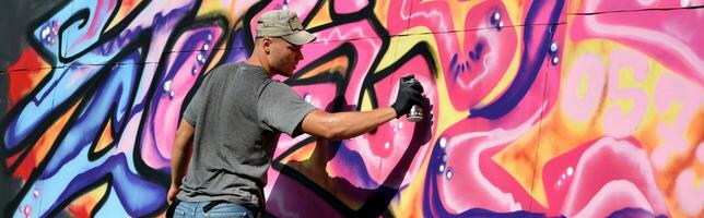 jovem caucasiano masculino grafite artista desenhando grande rua arte pintura dentro azul e Rosa tons foto