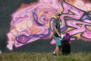 jovem caucasiano masculino grafite artista desenhando grande rua arte pintura dentro azul e Rosa tons foto