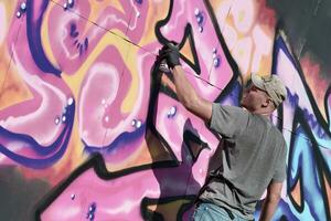 jovem caucasiano masculino grafite artista desenhando grande rua arte pintura dentro azul e Rosa tons foto