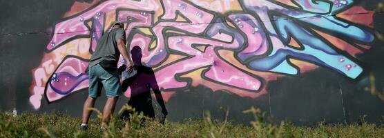 jovem caucasiano masculino grafite artista desenhando grande rua arte pintura dentro azul e Rosa tons foto