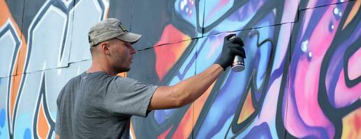 jovem caucasiano masculino grafite artista desenhando grande rua arte pintura dentro azul e Rosa tons foto