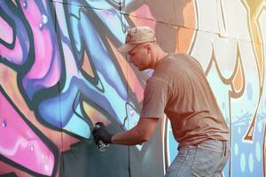 jovem caucasiano masculino grafite artista desenhando grande rua arte pintura dentro azul e Rosa tons foto