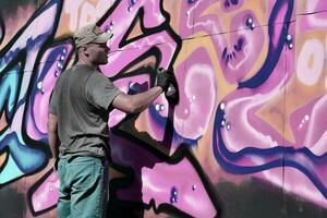 jovem caucasiano masculino grafite artista desenhando grande rua arte pintura dentro azul e Rosa tons foto