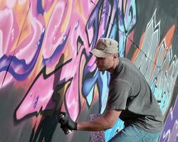jovem caucasiano masculino grafite artista desenhando grande rua arte pintura dentro azul e Rosa tons foto
