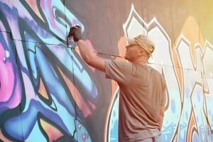 jovem caucasiano masculino grafite artista desenhando grande rua arte pintura dentro azul e Rosa tons foto