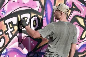 jovem caucasiano masculino grafite artista desenhando grande rua arte pintura dentro azul e Rosa tons foto