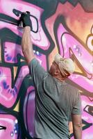 jovem caucasiano masculino grafite artista desenhando grande rua arte pintura dentro azul e Rosa tons foto