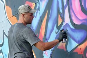 jovem caucasiano masculino grafite artista desenhando grande rua arte pintura dentro azul e Rosa tons foto