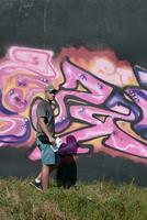 jovem caucasiano masculino grafite artista desenhando grande rua arte pintura dentro azul e Rosa tons foto