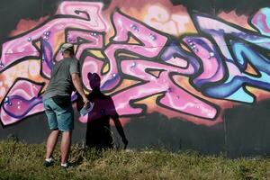 jovem caucasiano masculino grafite artista desenhando grande rua arte pintura dentro azul e Rosa tons foto