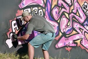 jovem caucasiano masculino grafite artista desenhando grande rua arte pintura dentro azul e Rosa tons foto