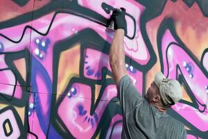 jovem caucasiano masculino grafite artista desenhando grande rua arte pintura dentro azul e Rosa tons foto