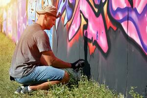 jovem caucasiano masculino grafite artista desenhando grande rua arte pintura dentro azul e Rosa tons foto