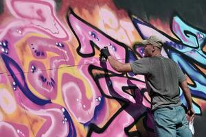 jovem caucasiano masculino grafite artista desenhando grande rua arte pintura dentro azul e Rosa tons foto