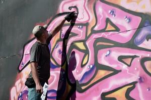 jovem caucasiano masculino grafite artista desenhando grande rua arte pintura dentro azul e Rosa tons foto