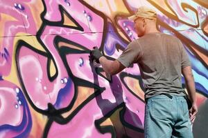 jovem caucasiano masculino grafite artista desenhando grande rua arte pintura dentro azul e Rosa tons foto