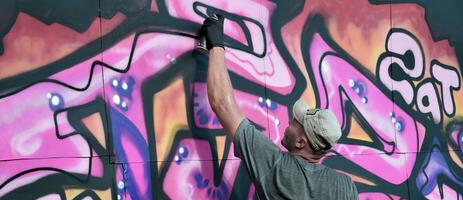 jovem caucasiano masculino grafite artista desenhando grande rua arte pintura dentro azul e Rosa tons foto