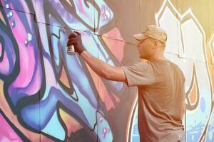 jovem caucasiano masculino grafite artista desenhando grande rua arte pintura dentro azul e Rosa tons foto