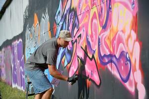 jovem caucasiano masculino grafite artista desenhando grande rua arte pintura dentro azul e Rosa tons foto