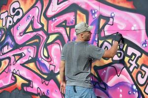 jovem caucasiano masculino grafite artista desenhando grande rua arte pintura dentro azul e Rosa tons foto