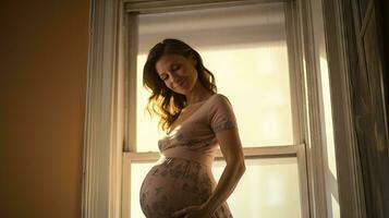 uma grávida mulher ficou sorridente dentro a canto do a janela com luz transmissão através a janela. foto