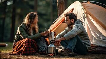 jovem casal tendo uma piquenique sentado perto uma fogueira e barraca beber café dentro a pinho floresta foto