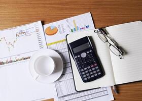 conceito de negócio com mesa de trabalho de madeira e xícara de café vazia, calculadora e caderno no relatório de documento foto