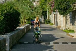 uma mulher com uma mochila caminhando com uma carrinho de criança dentro uma recorrer Cidade dentro Montenegro. foto