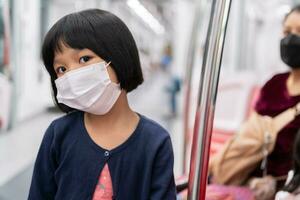 menina com máscara cirúrgica proteção facial contra gripe e surto de vírus em transporte público skytrain ou metrô. conceito de novo estilo de vida normal, usando o transporte público para viajar para a escola. foto