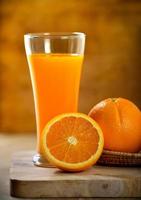 copo de suco de laranja e laranjas frescas na madeira foto
