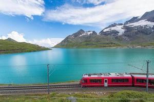 trem vermelho nas altas montanhas dos Alpes suíços passa perto de um lago foto