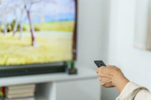 idosos mulher assistindo inteligente televisão e usando controlo remoto controlador mão segurando televisão audio controlo remoto ao controle meio era ásia mulher filme televisão Series gastos Tempo às casa foto