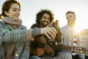 três feliz amigos com guitarra brindar Cerveja garrafas às pôr do sol foto