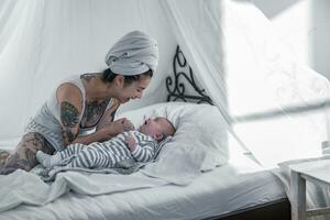 tatuado jovem mulher com dela bebê dentro marquise cama foto