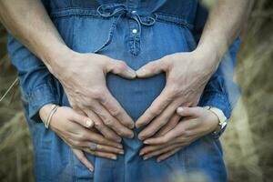 mão do homem formando coração em a barriga do dele grávida namorada foto