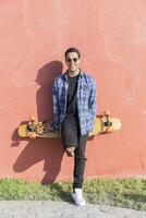 retrato do rindo jovem homem com Longboard em pé dentro frente do Rosa parede foto