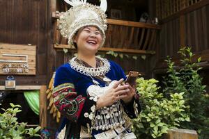 China, guizhou, rindo miao mulher vestindo tradicional vestir e cocar segurando célula telefone foto