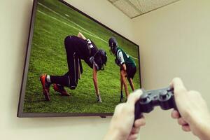 homem jogando vídeo jogo. mãos segurando console controlador. futebol ou futebol jogos em a televisão. panorâmico televisão carrinhos em cômoda. foto