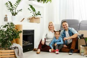 feliz família sentado em de madeira chão. pai, mãe e criança tendo Diversão junto. comovente casa dia, Novo casa e Projeto interior conceito foto