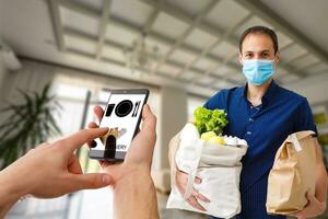 Entrega Comida serviço às lar. homem correio entregue a ordem não nome saco com Comida. mão segurando inteligente telefone com Comida conectados dispositivo em tela foto