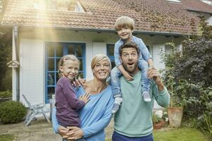 retrato do feliz família com dois crianças dentro frente do seus casa foto