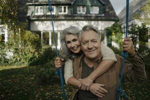 retrato do uma feliz mulher abraçando Senior homem em uma balanço dentro jardim foto