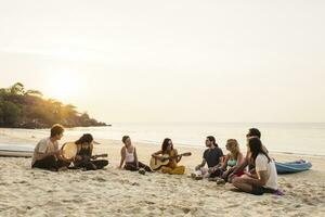 tailândia, koh Fangan, grupo do pessoas sentado em uma de praia com guitarra às pôr do sol foto