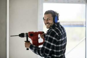 retrato do sorridente trabalhador usando elétrico broca em uma construção local foto