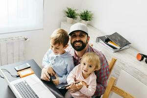 pai trabalhando às lar, usando computador portátil com dele crianças em dele colo foto