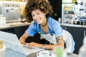 feliz fêmea proprietário usando computador portátil às contador dentro café fazer compras foto