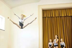 menina dentro ginástica equipamento fazendo aéreo saltar com três meninas assistindo foto